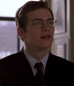 a young man wearing glasses and a suit in front of a window looking off to the side