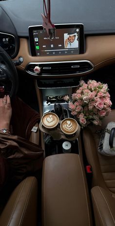 the interior of a car with two cups of coffee in front of it and a woman holding her phone