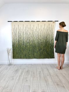 a woman standing in front of a wall hanging with grass on it and another painting behind her