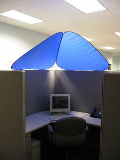 an office cubicle with a computer on the desk and a blue shade over it