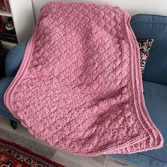 a pink crocheted blanket sitting on top of a blue couch next to a rug