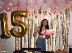 a woman holding a cake in front of balloons and streamers with the number fifteen on it