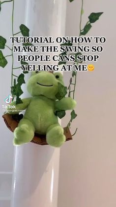 a green stuffed animal sitting on top of a white pole next to a potted plant