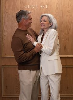 an older man and woman standing next to each other in front of a wooden wall