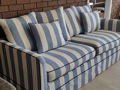 a blue and white striped couch sitting on top of a hard wood floor next to a brick wall