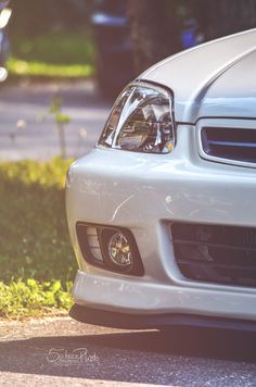 the front end of a white car parked on the side of the road next to grass