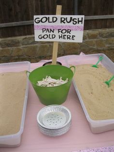 a table topped with lots of sand next to a sign that says gold rush pan for gold here