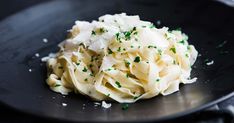 a black plate topped with pasta covered in parmesan cheese and green sprinkles