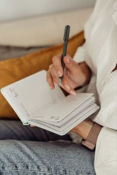 a person sitting on a couch holding a notebook and pen in their hand while writing