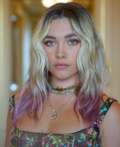 a woman with blonde hair and blue eyes wearing a floral top is looking at the camera