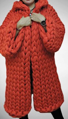 a woman in an orange knitted coat with her hands on her chest, posing for the camera