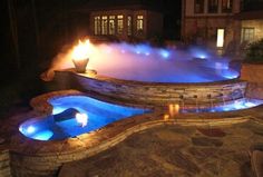 an outdoor hot tub lit up at night with blue lights on the side and water coming out from it