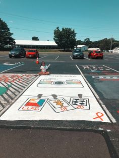 a woman sitting on the side of a parking lot next to a large chalk drawing