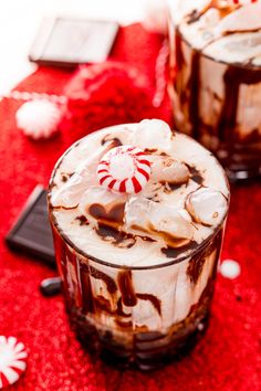 two glasses filled with hot chocolate and marshmallows on top of a red table