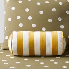 a pillow on a bed with white and yellow striped pillows in front of polka dot wallpaper