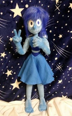 a stuffed animal doll with blue hair and stars around her body, making the peace sign