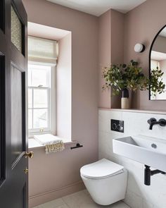 a white toilet sitting next to a bathroom sink under a mirror and a potted plant