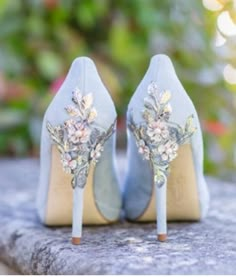 a pair of blue high heel shoes with flowers on the heels are sitting on a stone surface