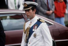 a man in uniform standing next to a car with other people watching him from behind