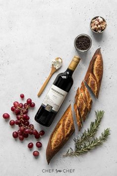 an assortment of breads and wine on a table with grapes, nuts and herbs