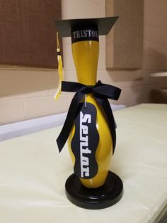 a yellow vase with a black ribbon around it's neck and name on the top