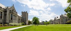 people are walking on the grass in front of an old building with tall towers and windows