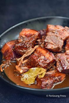 some meat and sauce in a black bowl on a blue tablecloth with a spoon