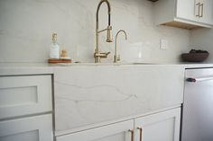 a white kitchen with marble counter tops and gold faucet, sink, dishwasher and refrigerator