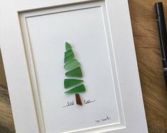 a paper cut christmas tree sitting on top of a wooden table next to a pen