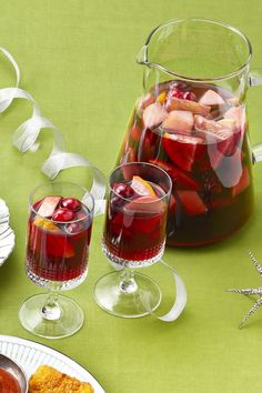 a pitcher of water and two glasses filled with liquid on top of a green table