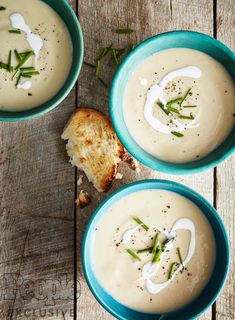 two blue bowls filled with soup on top of a wooden table next to a piece of bread