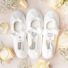 three pairs of white baby shoes with bows and name tags on them next to flowers