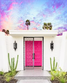 a pink door is in front of a white house with cactus plants and palm trees