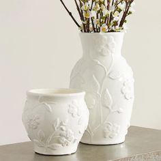 two white vases with flowers in them sitting on a table next to each other