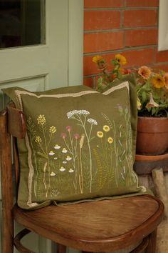 a pillow sitting on top of a wooden chair next to a potted flower plant