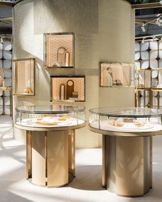 two round tables with glass tops in a room filled with white and gold objects on display