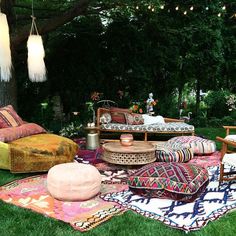 an outdoor seating area with colorful pillows and rugs on the grass, surrounded by trees