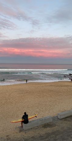 a person sitting on a bench at the beach with a surfboard in front of them