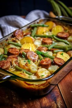 a casserole dish with sausage, potatoes and green beans on a wooden table