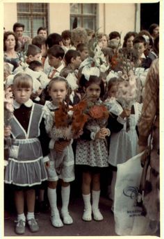 an old black and white photo of children holding flowers in front of a group of people