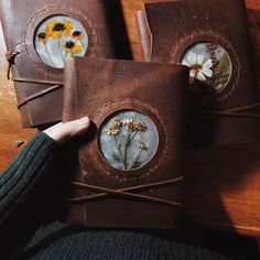 a person holding three brown leather journals with flowers on them