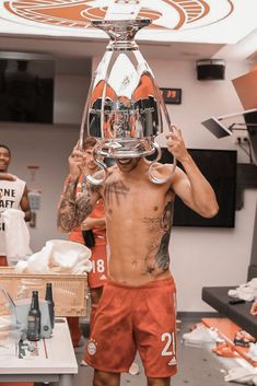 a shirtless man holding up a trophy in front of his face while other men look on