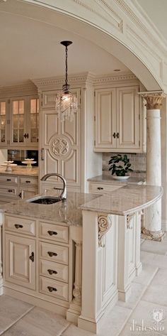 a large kitchen with marble counter tops and white cabinets, along with an archway leading to the dining room