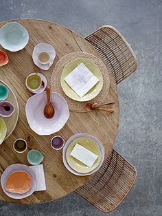 a wooden table topped with white plates and bowls next to a brown wicker chair