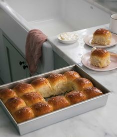 rolls in a pan on a kitchen counter next to two plates with cream cheeses