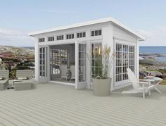 a small white house sitting on top of a wooden deck next to the ocean with chairs and tables