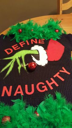 there is a black sweater with green feathers on it and the words define naughy