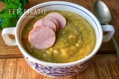 a close up of a bowl of soup on a wooden table with spoon and parsley