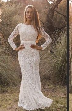 a woman standing in the grass wearing a white lace dress with long sleeves and an open back