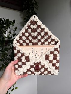 a hand holding an envelope made out of crocheted material with a brown and white checkerboard pattern